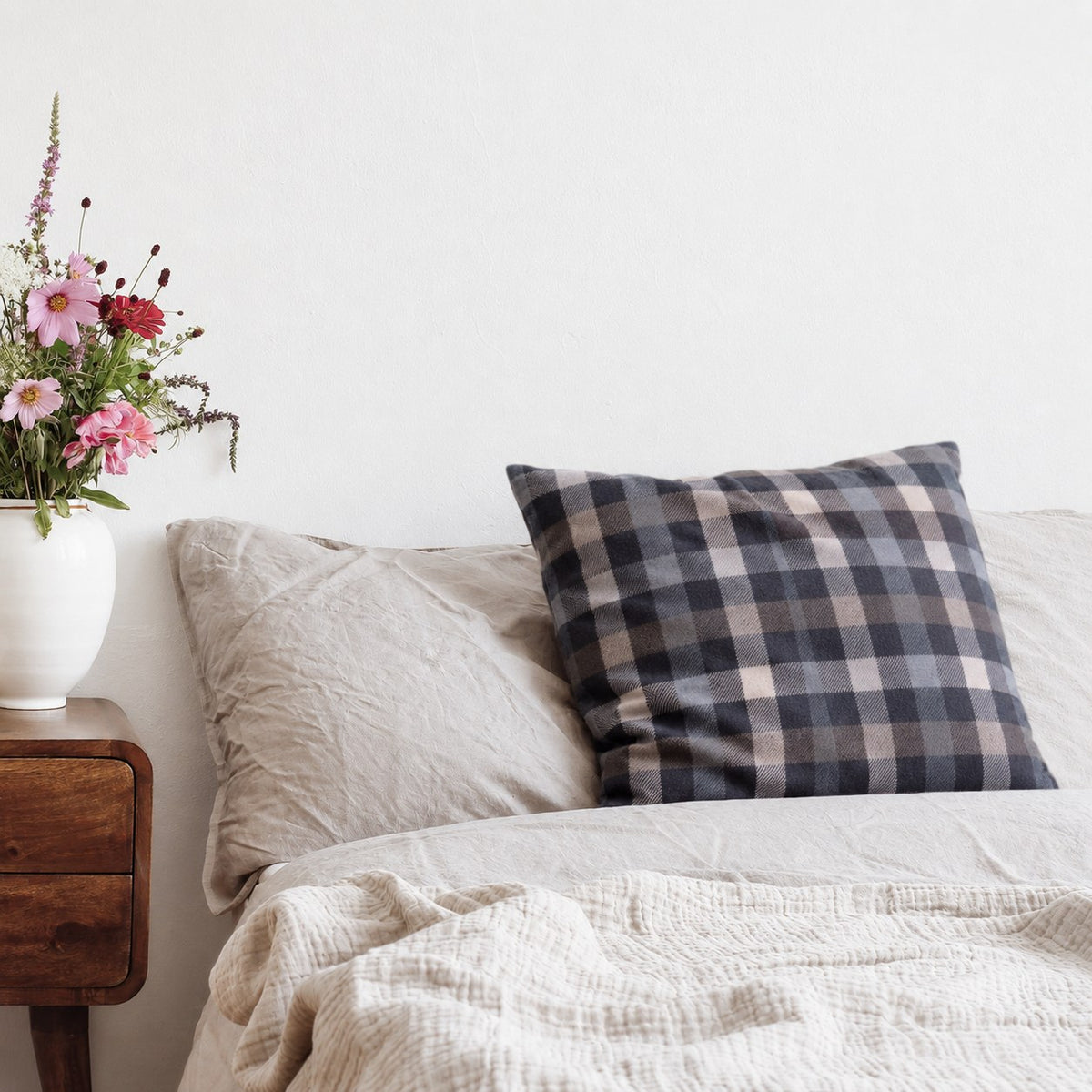 Kissen mit Flanellbezug in Grau Kariert auf einem Bett neben einem Nachttisch mit Blumen