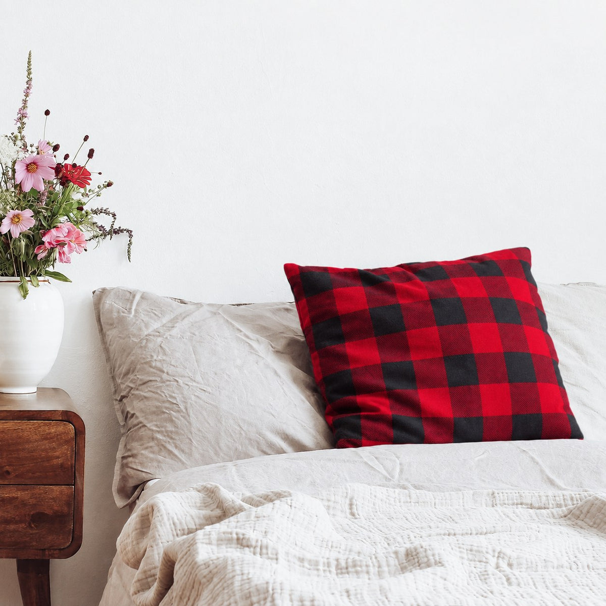 Kissen mit Flanellbezug in Rot Kariert auf einem Bett neben einem Nachttisch mit Blumen